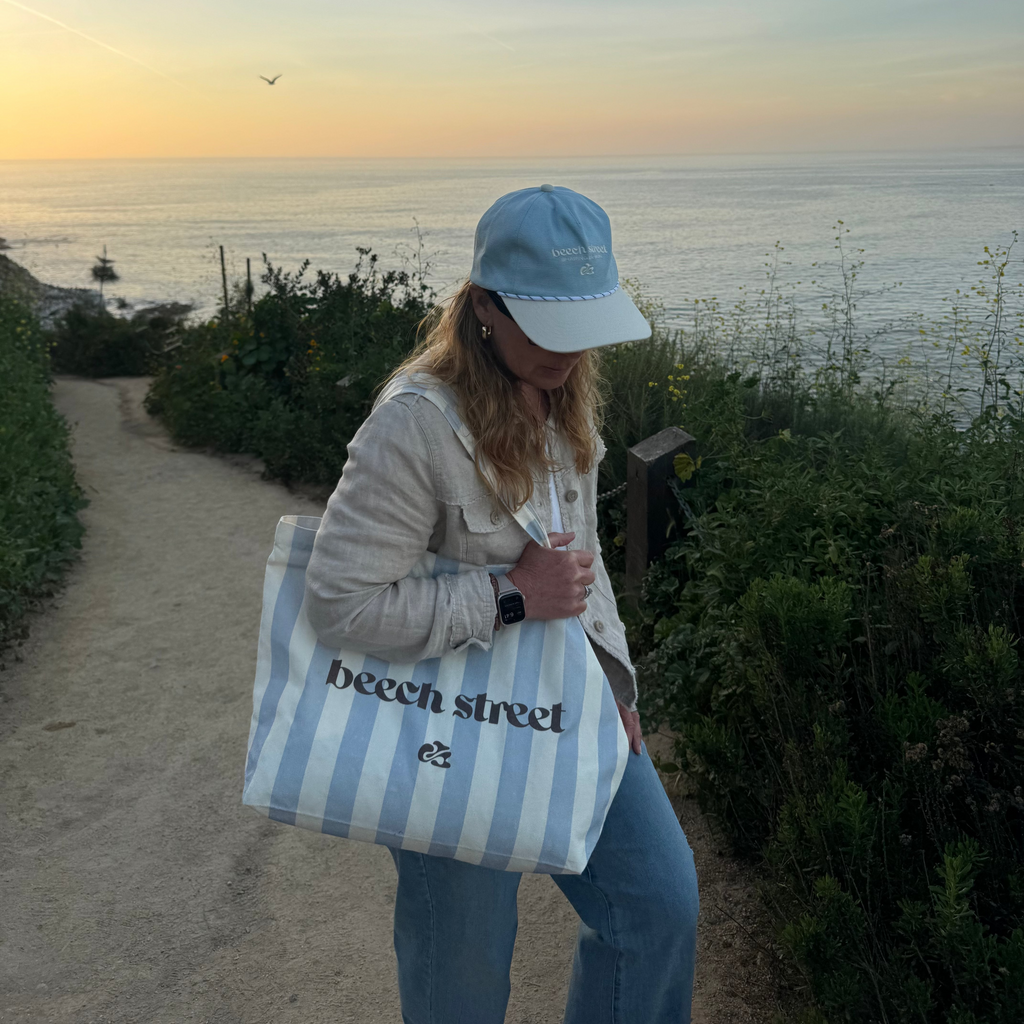 Person holding a striped bag with 'beach street' text by the ocean at sunset.