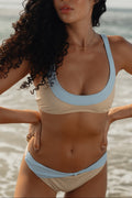 Woman in a beige and light blue bikini standing on a beach with ocean in the background