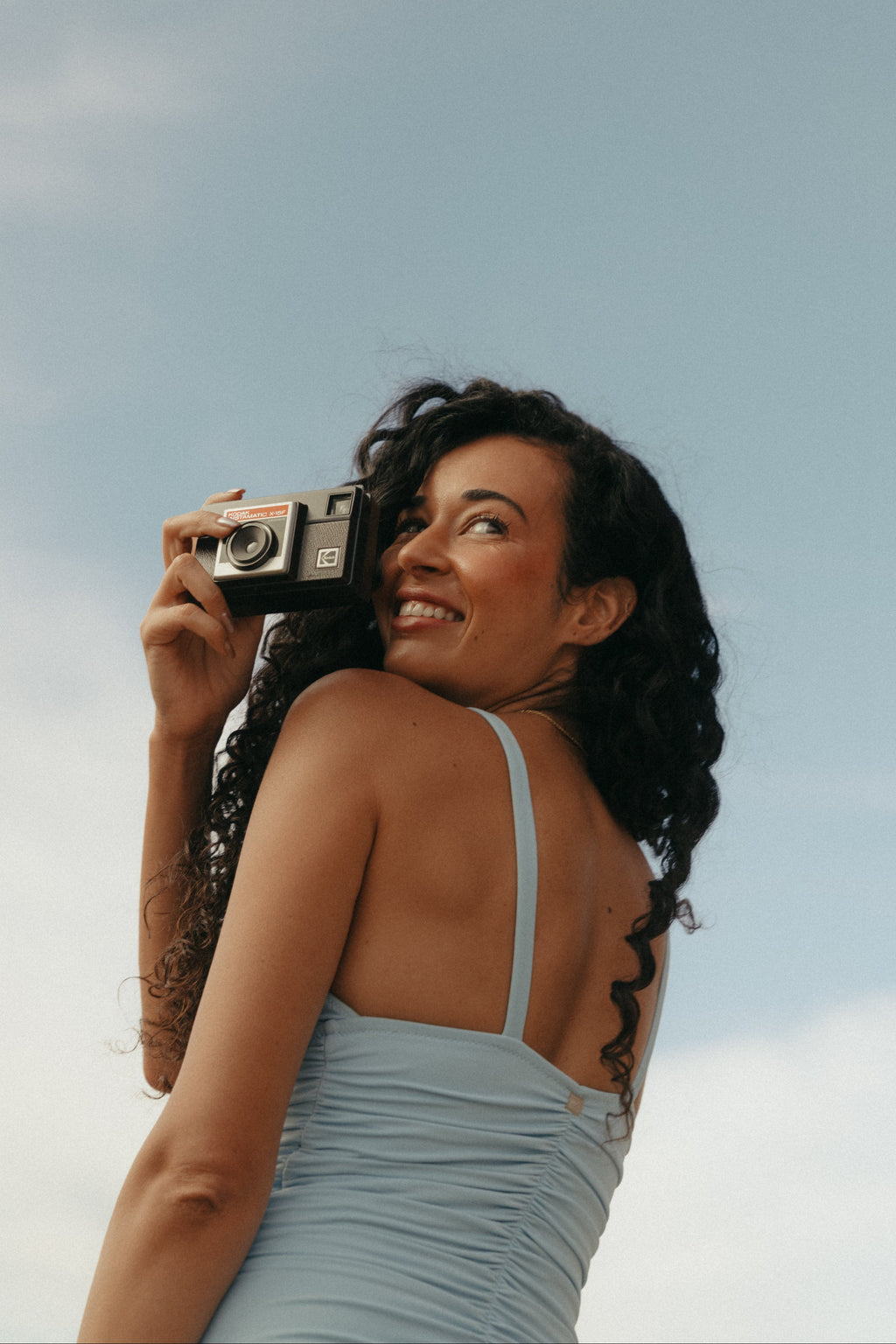 Woman taking a photo with a vintage camera against a clear sky