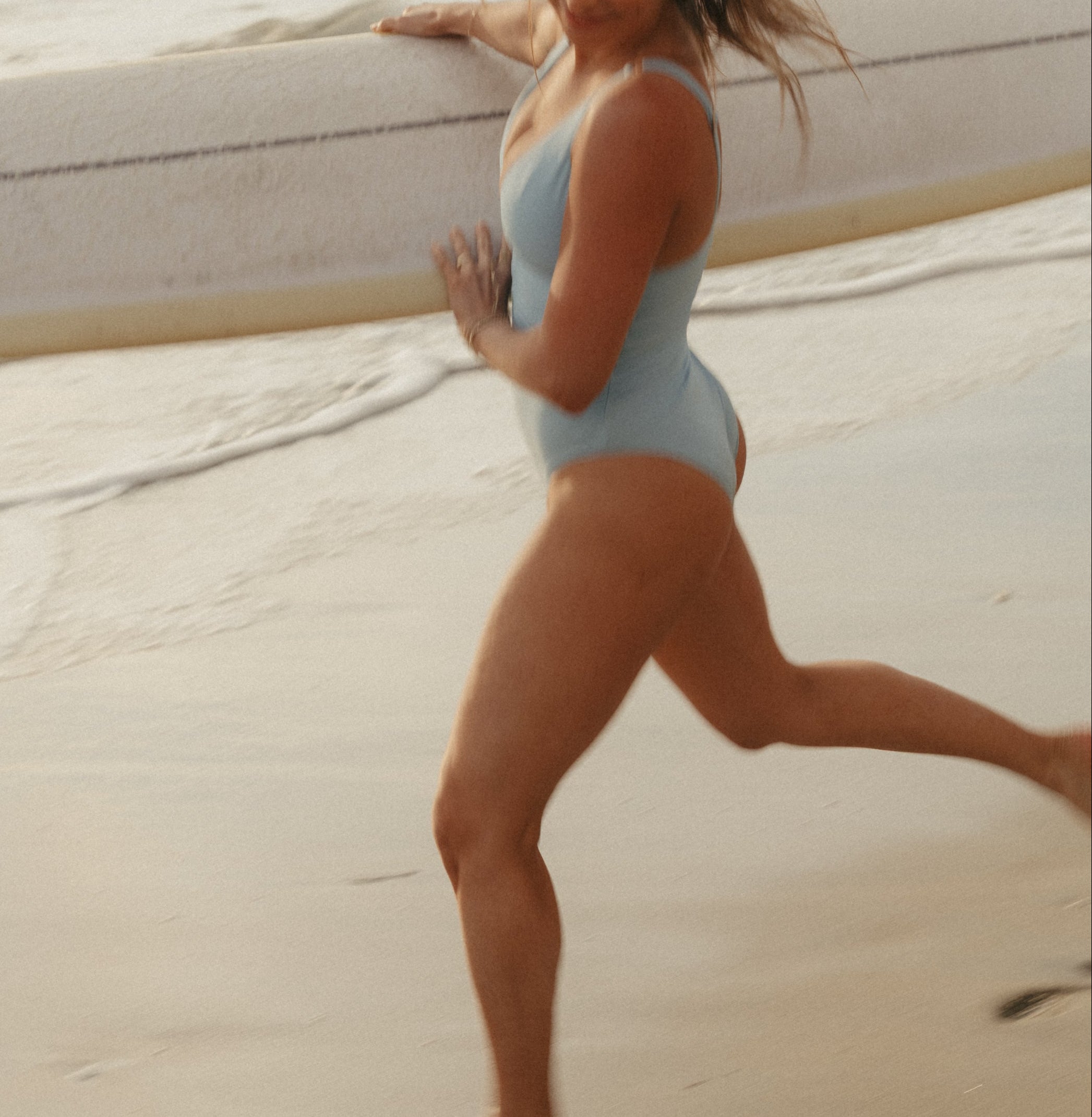 Woman in a light blue swimsuit standing on a beach with waves in the background
