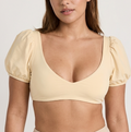 Woman wearing a yellow top and beige high-waisted bikini bottoms on a white background